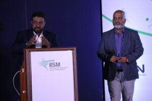 Mustafa Sapatwala speaking on the mic, while Amit Gupte is standing next to him.